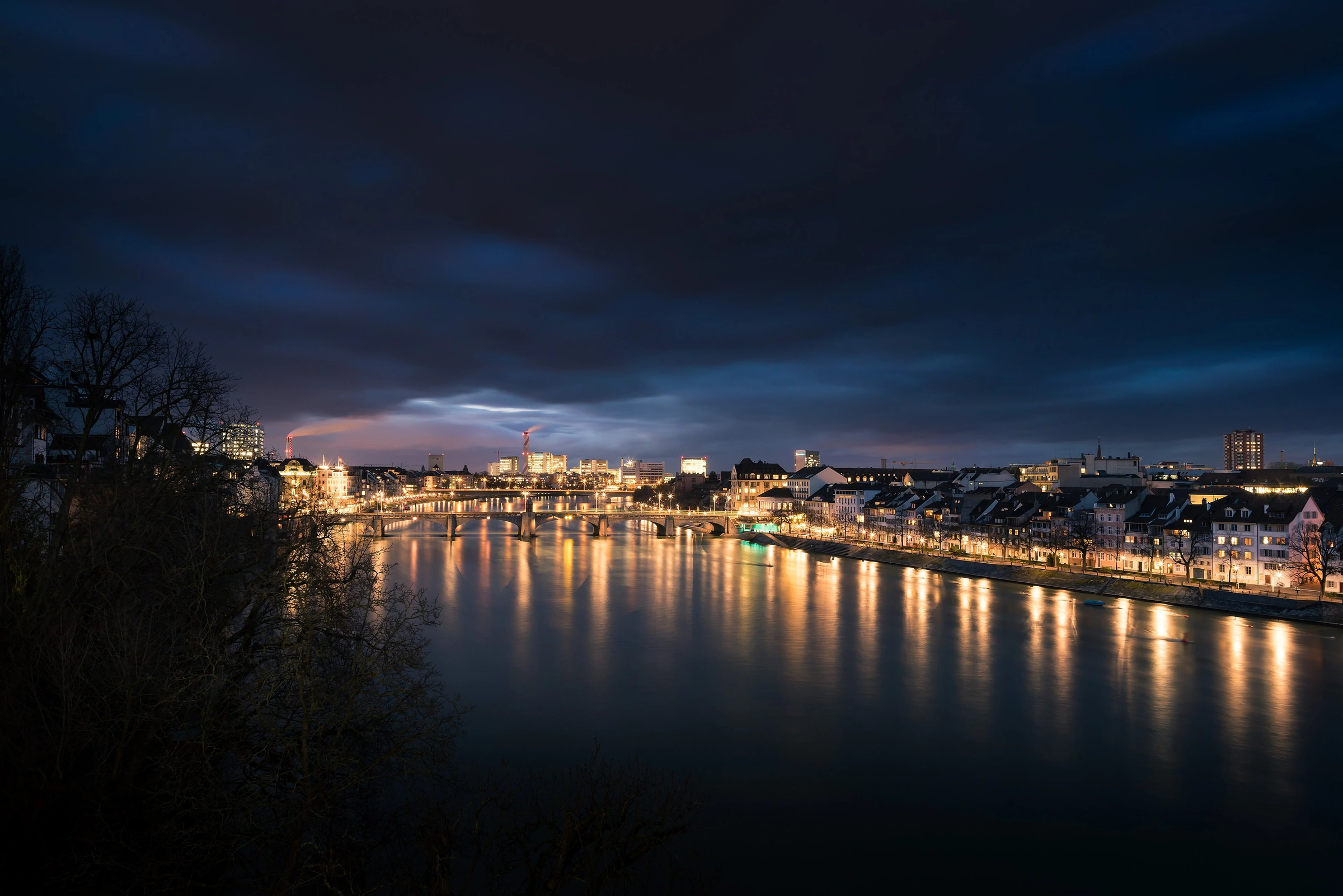 Basel at night from Münsterplatz, with the illuminated Middle Bridge, Rhine waterfront and long-exposure reflections.
