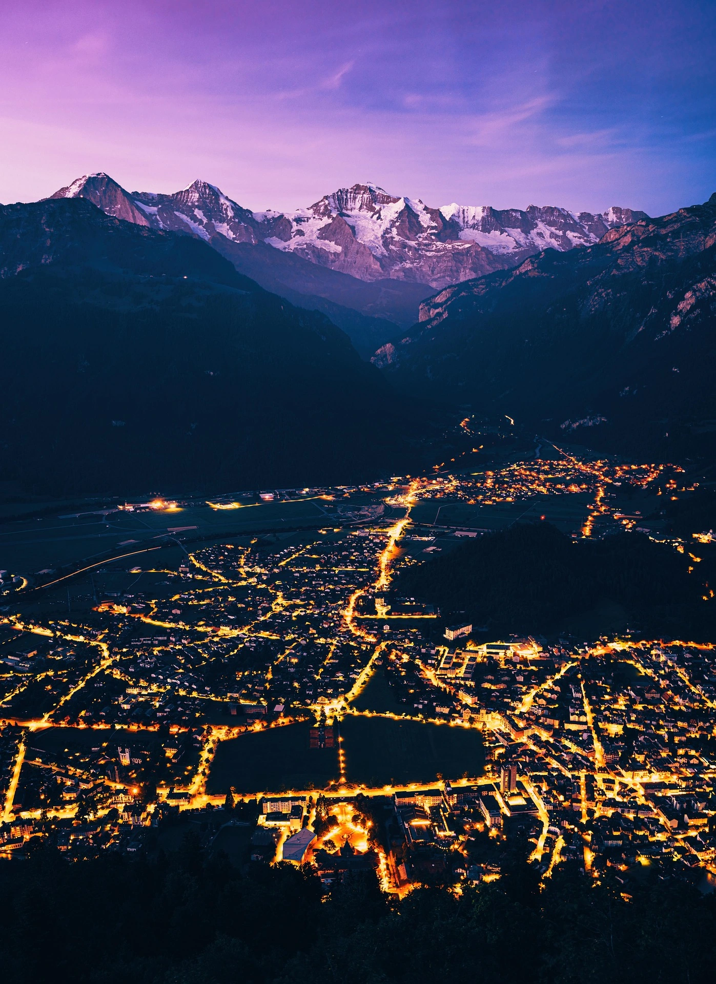 Interlaken and the illuminated Höhematte area beneath the Bernese Alps at night, photographed from above.