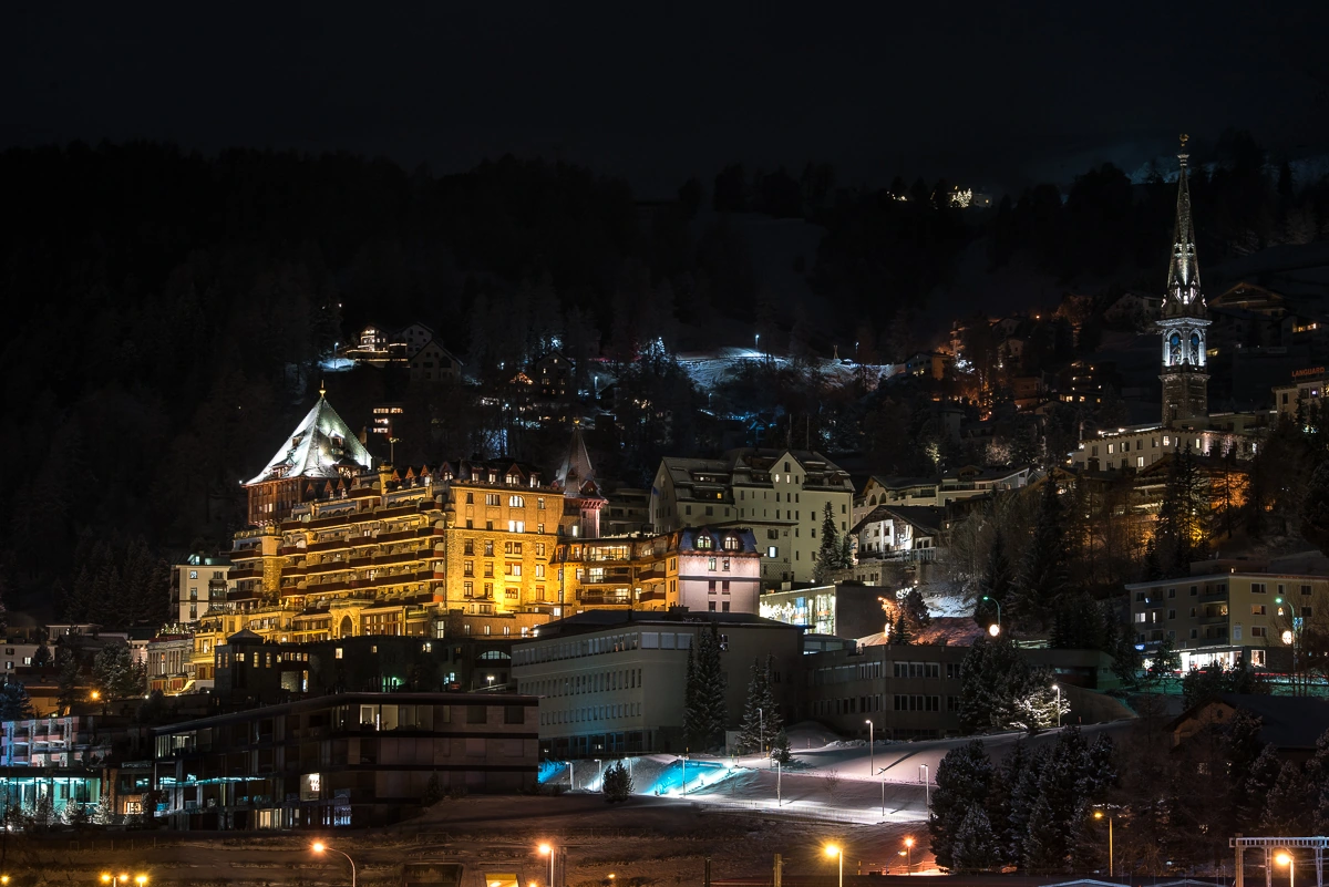 Badrutt’s Palace, St. Moritz village and the illuminated church on a winter night.