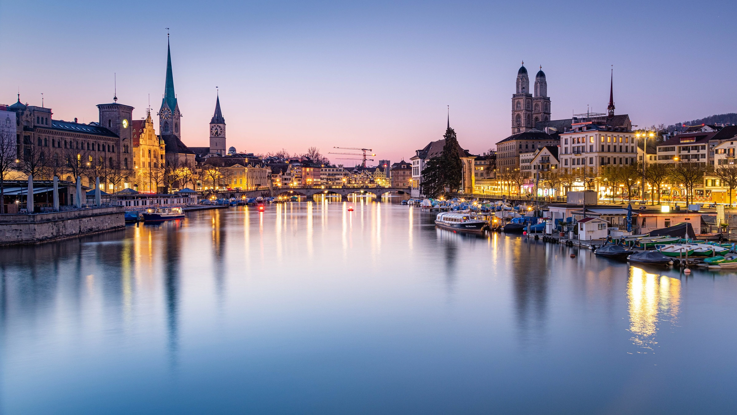 Zurich old town and the Limmat at blue hour, with illuminated church towers and reflections viewed from Quaibrücke.